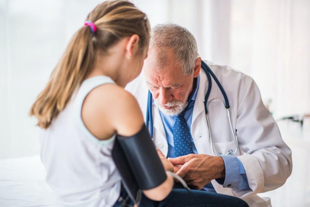 Senior doctor checking a small girl in his office.